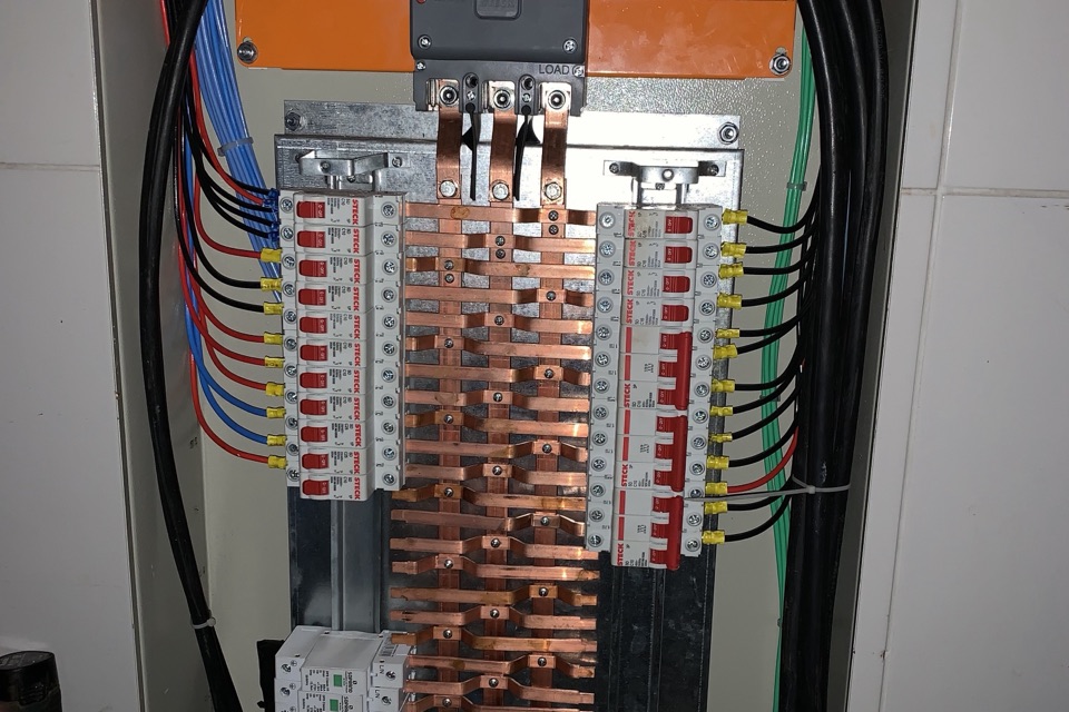 Quadro de distribuição elétrica aberto, com barramentos de cobre centrais e disjuntores organizados nas laterais.