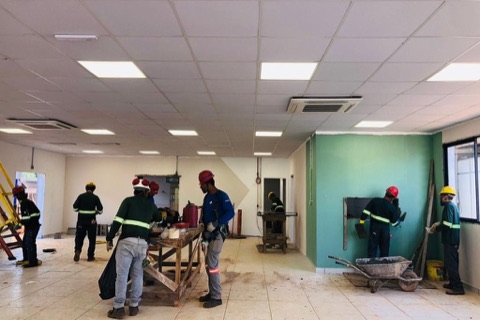 Equipe técnica em ambiente de obra multidisciplinar, com forro, ar-condicionado, pintura e acabamento em execução simultânea.