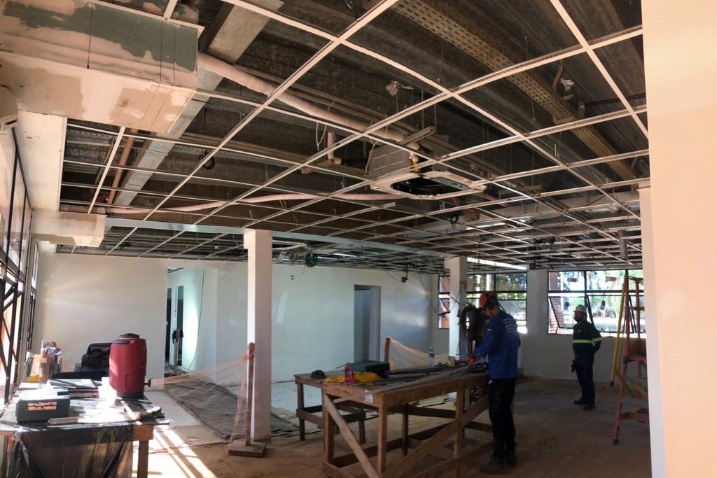 Estrutura metálica de forro modular instalada em teto de obra, com infraestrutura elétrica aparente e equipe técnica no ambiente.