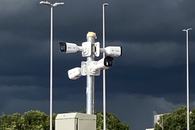 Câmeras de CFTV instaladas em poste metálico com caixa de conexão, em estacionamento.