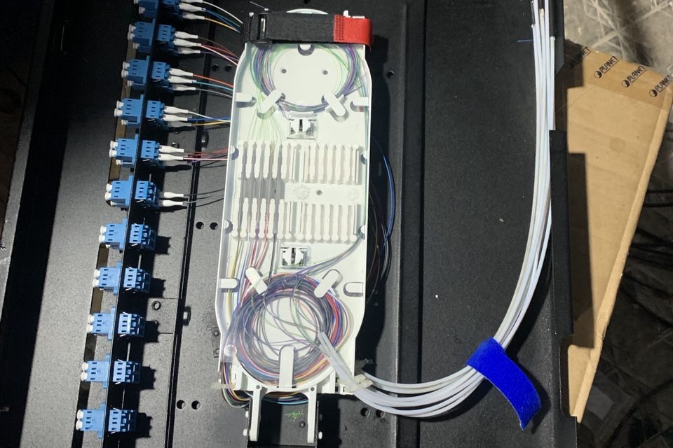 Distribuidor óptico aberto com bandeja de fusão e adaptadores de fibra conectados.