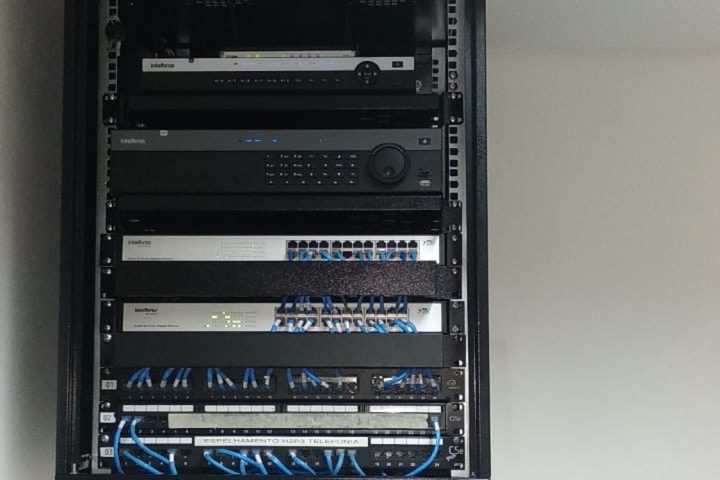 Rack fechado com switches, gravador e patch panels instalados em sequência.