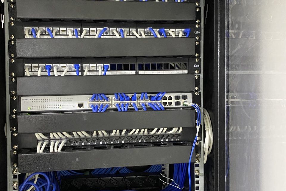 Rack de rede com organizadores verticais e cabos azuis passados de forma organizada.