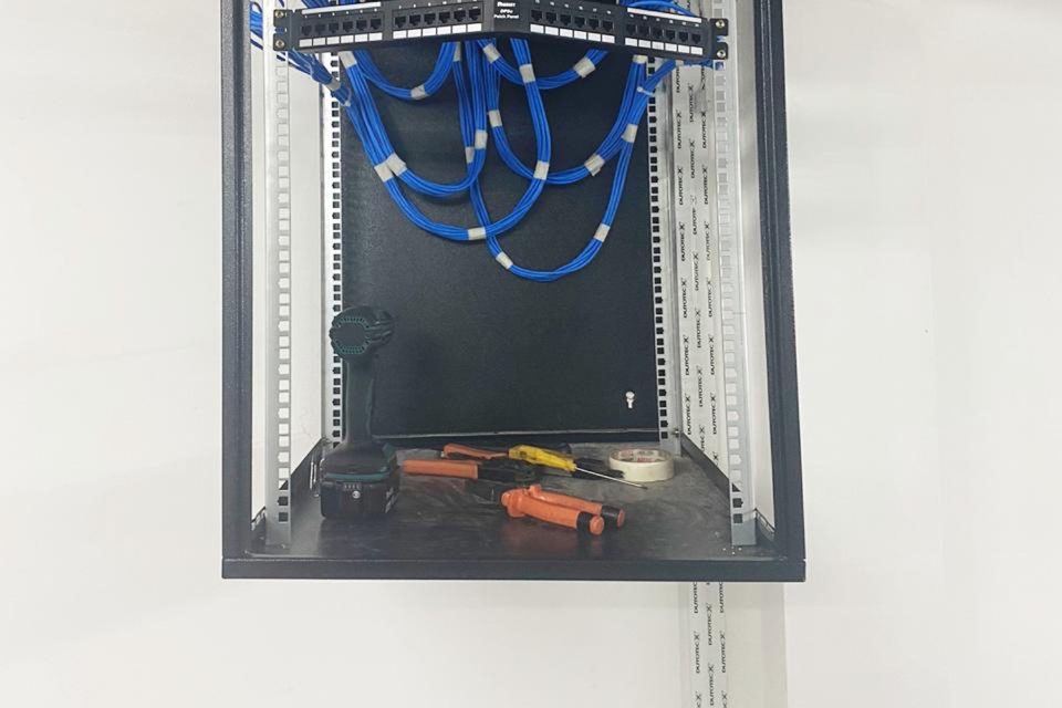 Rack de parede com patch panel e cabos azuis acomodados em organizador.