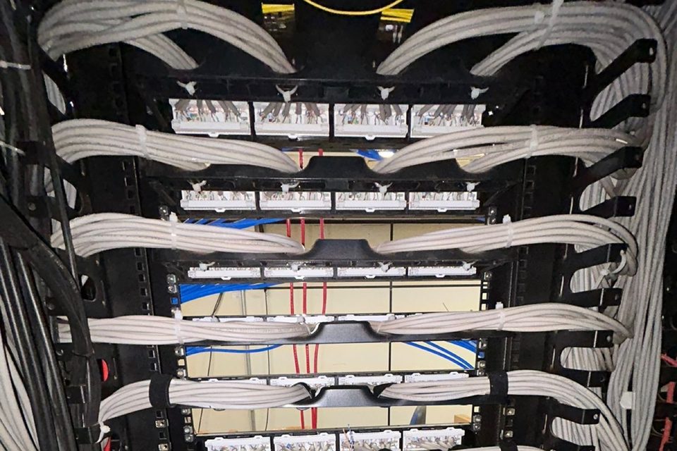 Rack com patch panels e cabos de rede passados em feixes organizados pelos guias laterais.