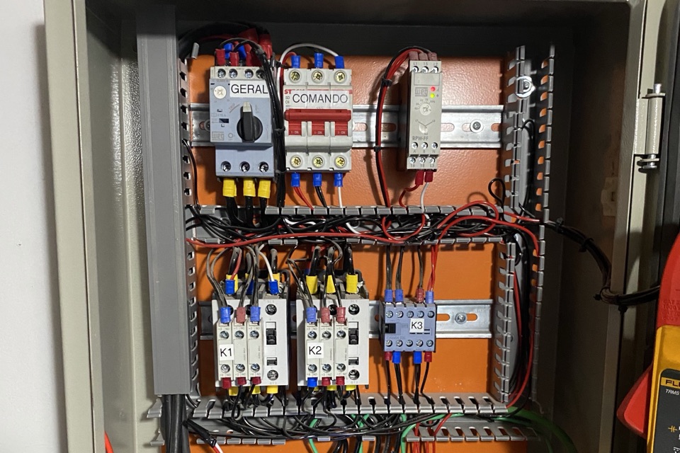 Painel de comando elétrico aberto, com contatores identificados, disjuntores de comando e fiação organizada.