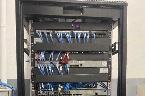 Rack de telecomunicações com patch panel Cat.6 e cabos de rede azuis organizados, switch de rede abaixo.