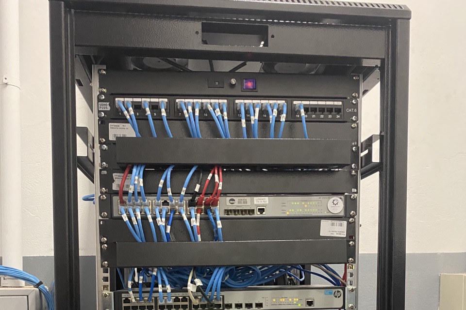 Rack de telecomunicações com patch panel Cat.6 e cabos de rede azuis organizados, switch de rede abaixo.